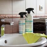 Eco-friendly cleaning products displayed on a bathroom sink with tiles and a basket.