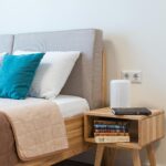 Comfortable bed covered with coverlet with soft pillows near stack of books on wooden bedside table